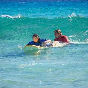 Surflehrer schiebt Surfschüler in die Wellen